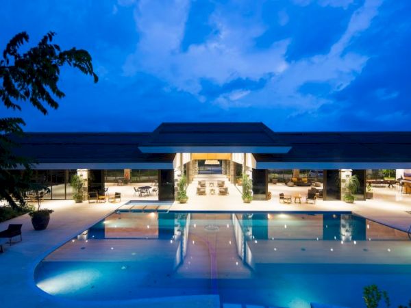 A luxurious residence features a large illuminated pool and spacious outdoor seating against a vibrant evening sky.