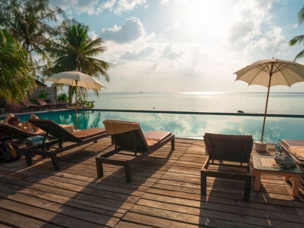 A serene poolside view with lounge chairs and umbrellas, overlooking a calm body of water beneath a partly cloudy sky.