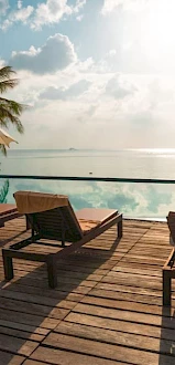 A serene poolside scene with lounge chairs, umbrellas, and a view of the ocean under a partly cloudy sky.