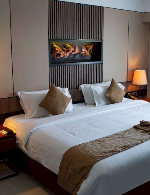 Image of a hotel room with a large bed, lamps, and a modern decor, featuring earth tones and a decorative towel on the bed.