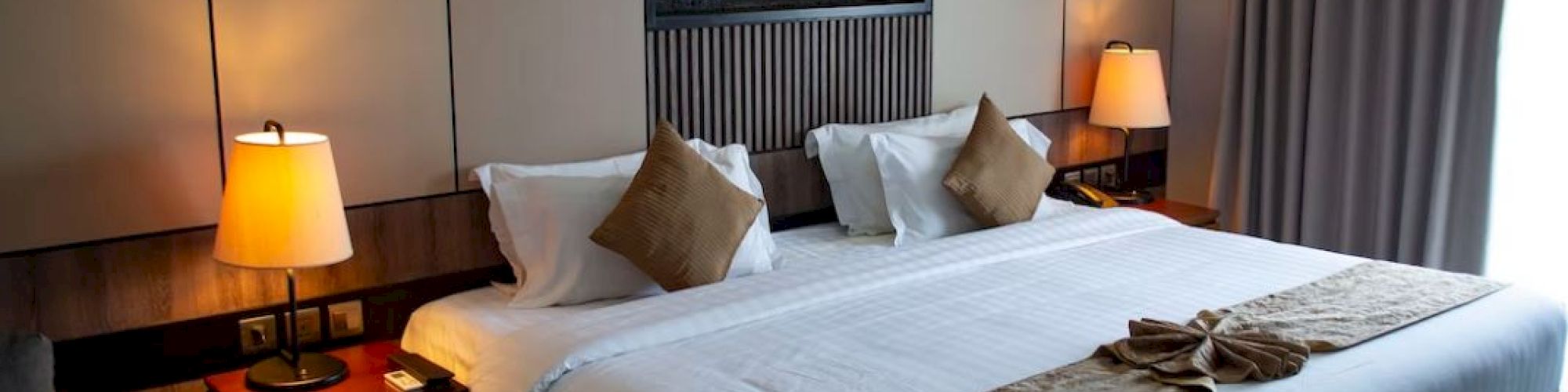 A cozy hotel room with a large bed, two lamps, and elegant decor, featuring a calming wall art piece for ambiance.