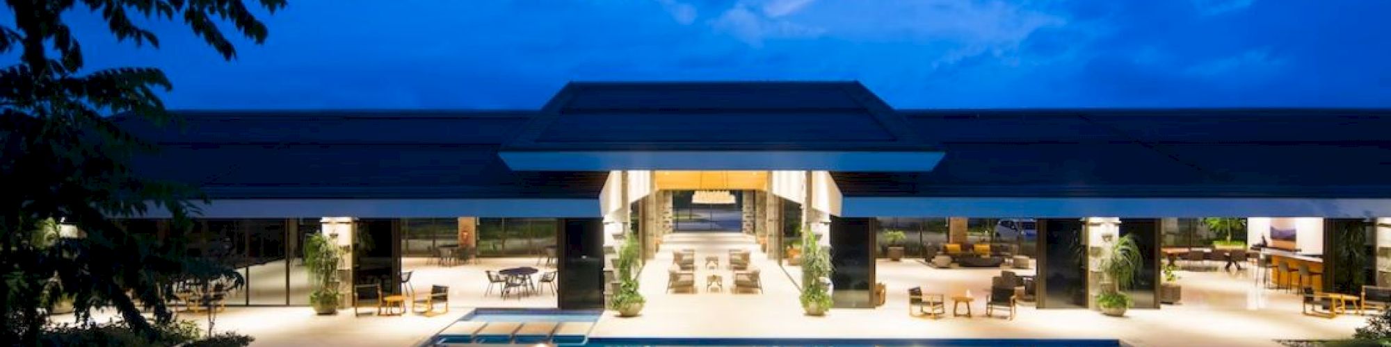 Luxurious building with an illuminated pool, surrounded by seating areas, under a twilight sky.