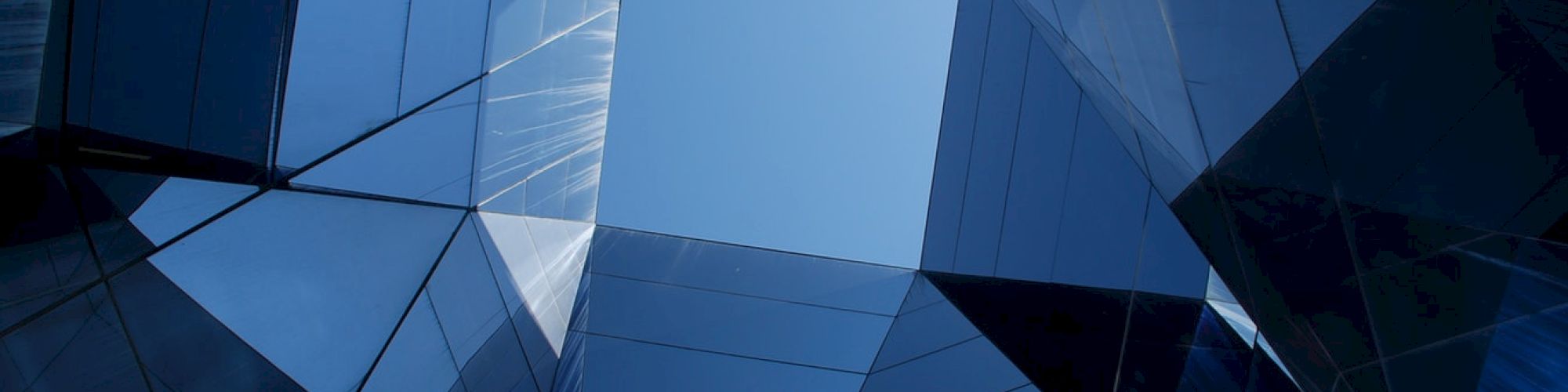 The image shows a geometric architectural structure with reflective glass panels, creating a symmetrical view of the sky at the center.