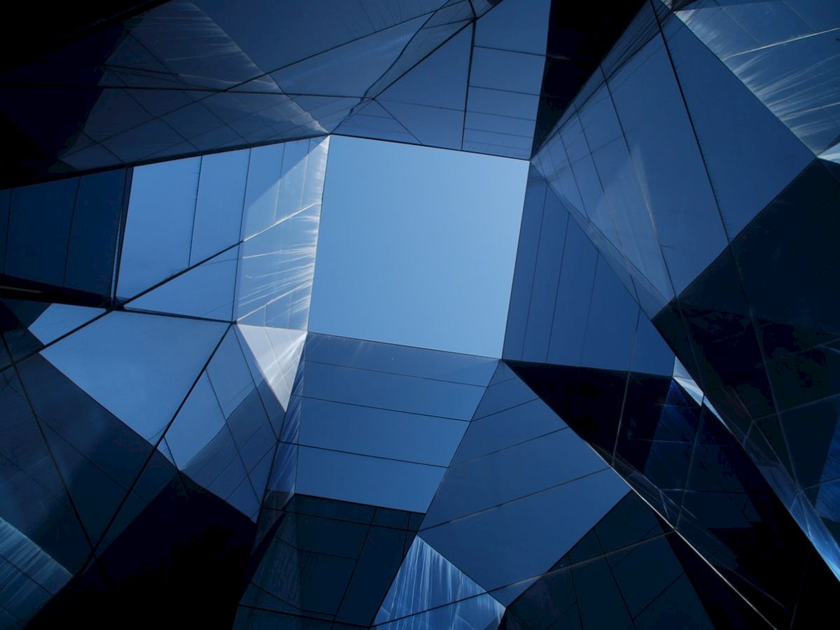 Geometric, reflective skyscrapers form a fragmented view toward the sky, creating an abstract architectural composition.