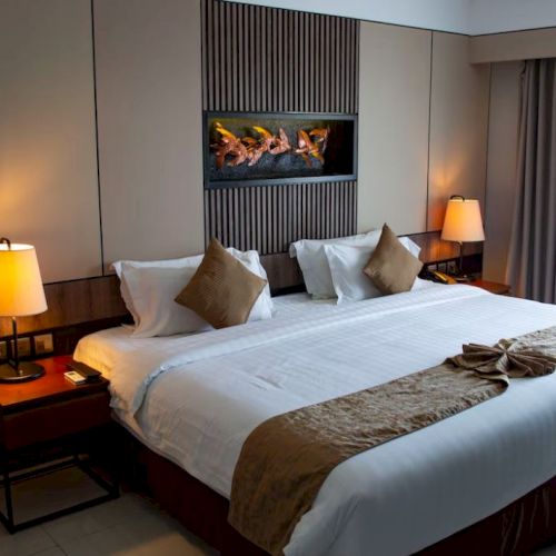 A cozy hotel room with a large bed, two side tables with lamps, and a decorative wall feature above. Soft lighting creates a warm ambiance.