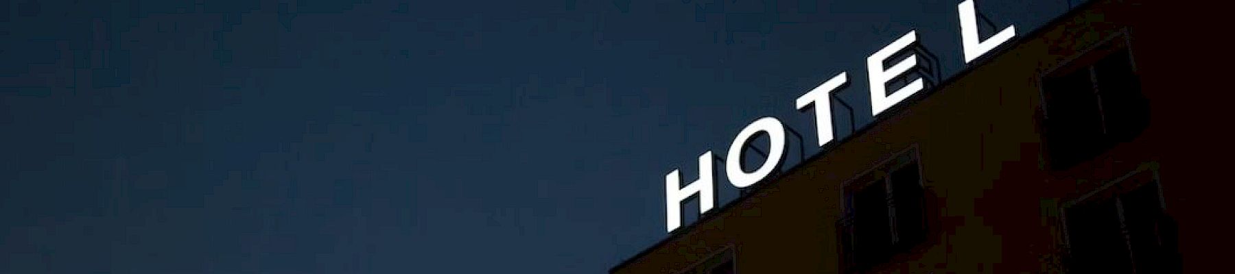 A building with a neon sign that reads "HOTEL" is set against a dark twilight sky, with some windows visible.