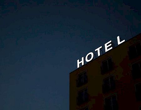A building with a neon sign that reads "HOTEL" is set against a dark twilight sky, with some windows visible.