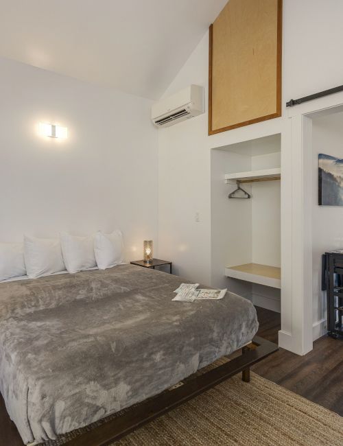 A bright modern bedroom with a queen bed, bedside lamps, an air conditioner, and a sliding barn door leading to the hallway.