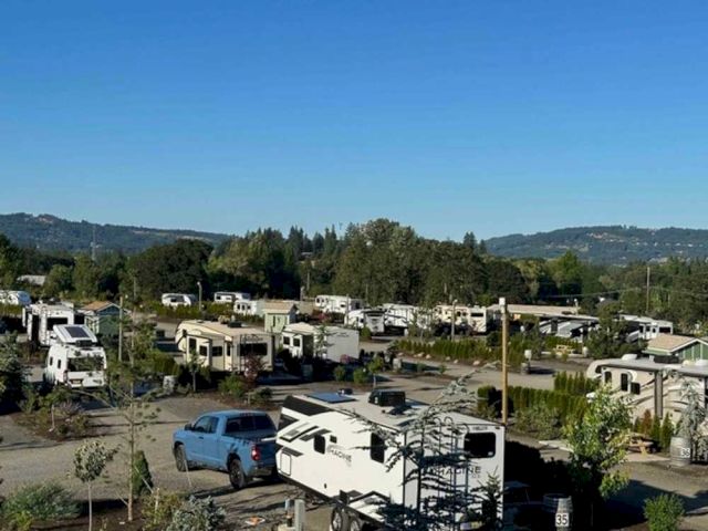 An RV park with multiple recreational vehicles and a truck, surrounded by greenery and hills under a clear blue sky.