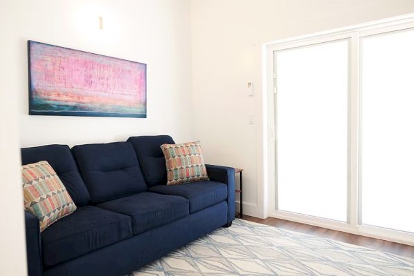 A cozy living room with a navy sofa, colorful cushions, abstract artwork, and large sliding glass doors letting in bright light.