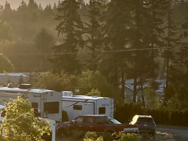 The image shows a scenic view with hot air balloons floating above trees, RVs, and cars in the foreground at sunset.