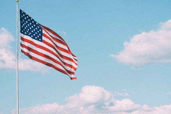 An American flag waving against a clear blue sky with a few clouds.