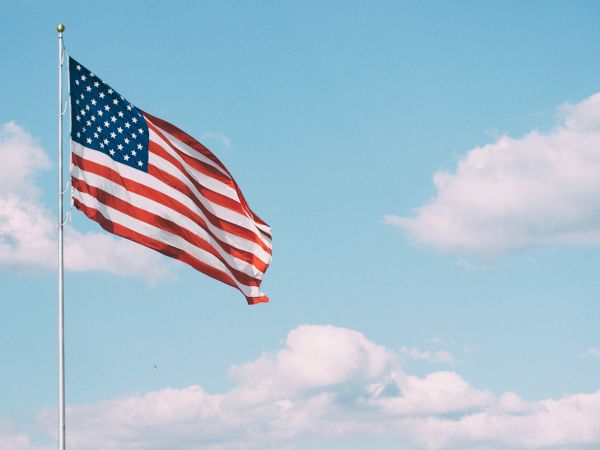 An American flag waving against a clear blue sky with a few clouds.