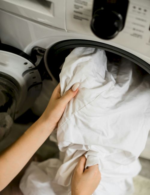 A person is placing white laundry into a front-loading washing machine.