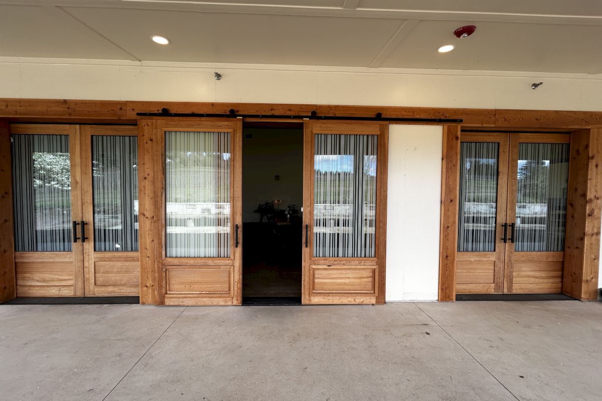The image shows wooden sliding doors with glass panels, leading to an indoor area with tables and chairs visible inside the room.