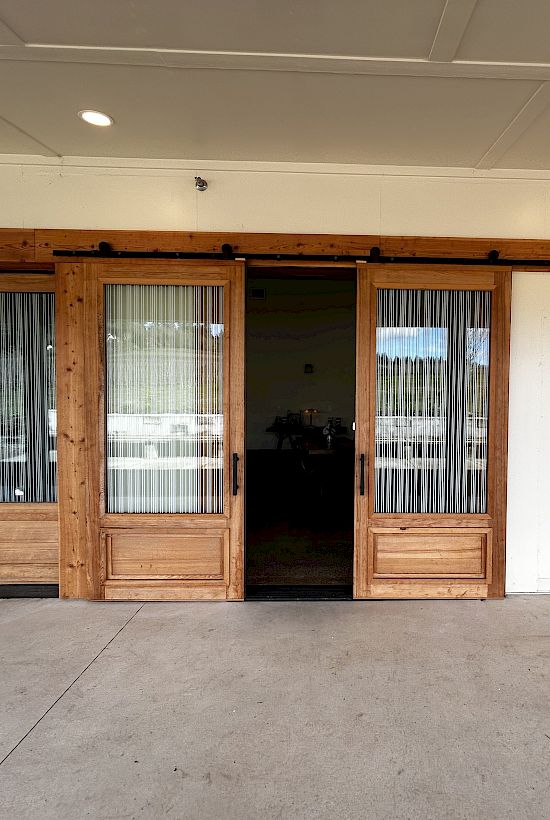 The image shows wooden sliding doors with glass panels, leading to an indoor area with tables and chairs visible inside the room.