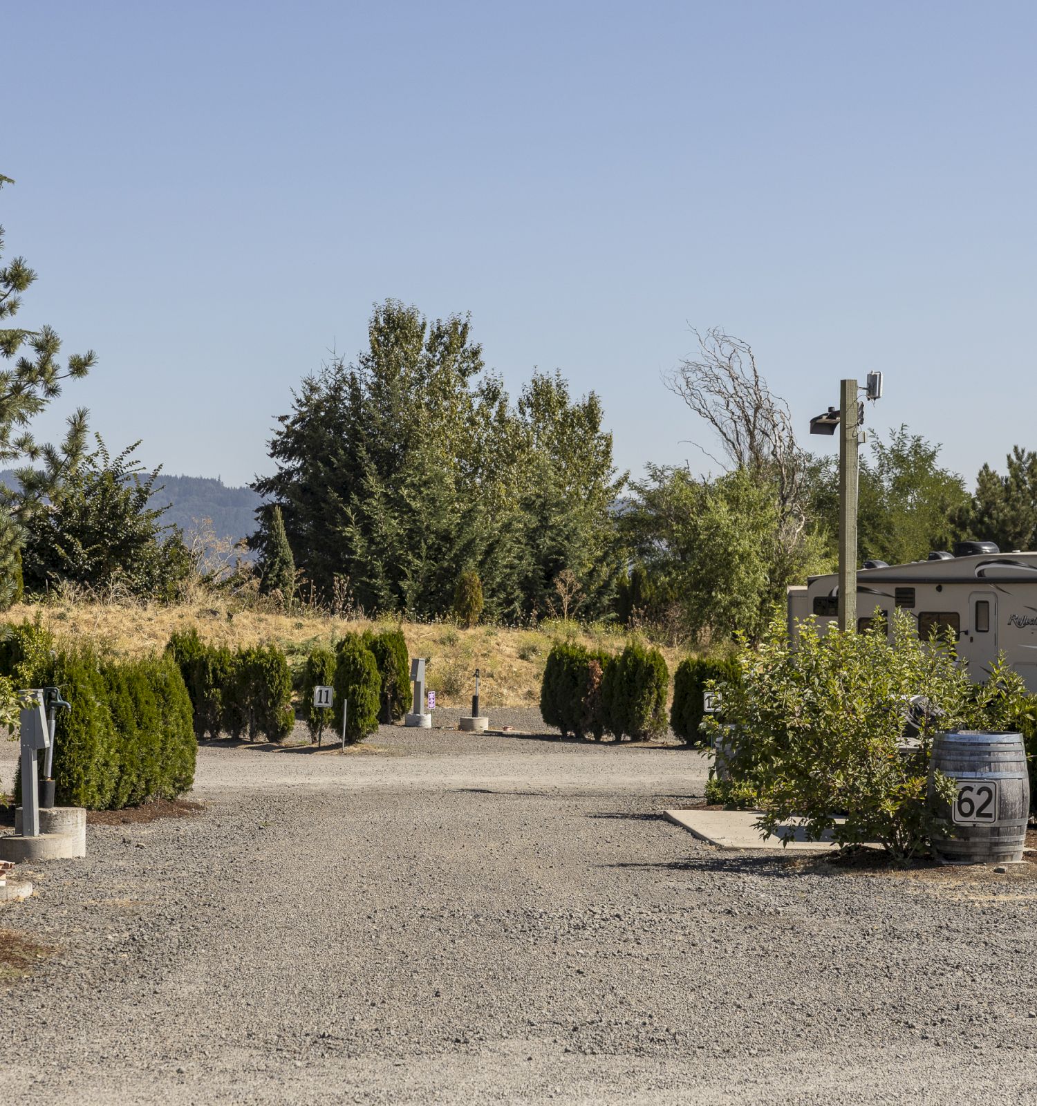 A camper trailer parked at a landscaped campground beside trees and a field under a clear blue sky.
