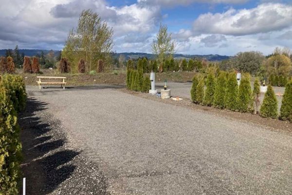 A gravel path leads through a landscaped area with small trees and a bench under a partly cloudy sky.