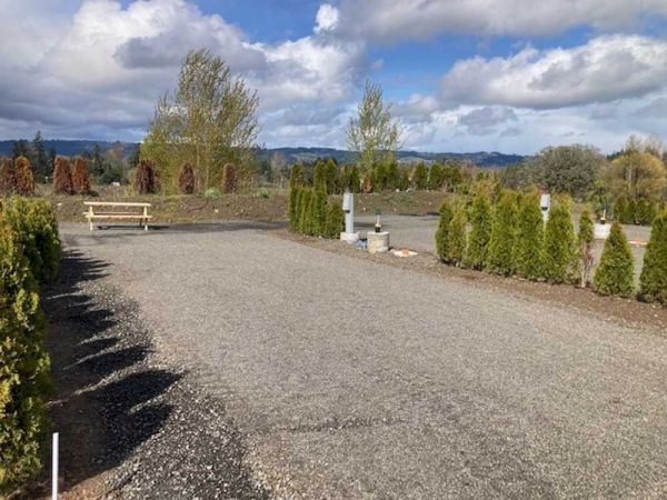 A gravel path leads through a landscaped area with small trees and a bench under a partly cloudy sky.