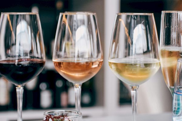 The image shows four wine glasses filled with different types of wine, arranged on a table with blurred shelves in the background.