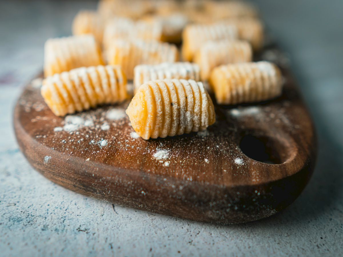 The image shows uncooked gnocchi arranged on a wooden cutting board dusted with flour, ready to be cooked.