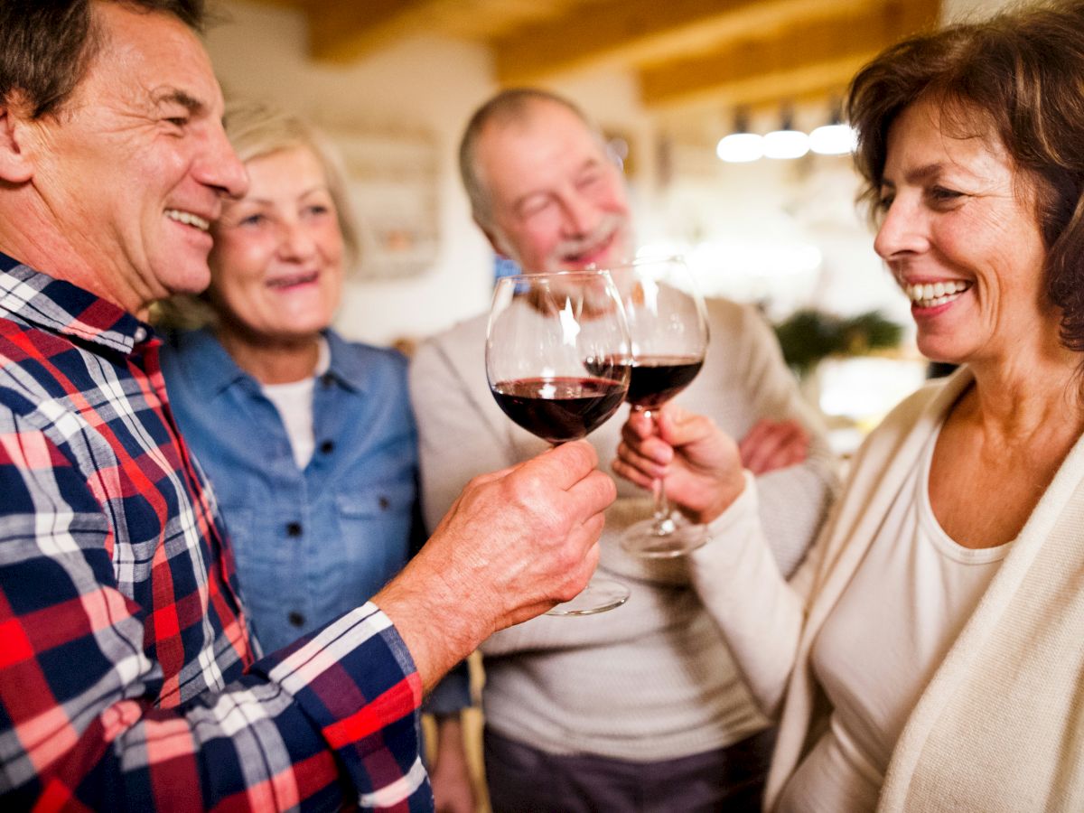 A group of four people enjoying a cheerful moment, clinking wine glasses, and smiling warmly at each other indoors.