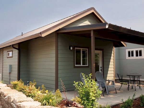 A modern home&rsquo;s exterior shows a covered entryway with a door, patio chairs, and small landscaped plants.