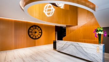 A modern interior with a marble desk, wooden accents, large clock, and decorative lights and flowers.