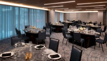 The image shows an elegantly set banquet hall with round tables, blue chairs, and floral centerpieces, ready for an event.