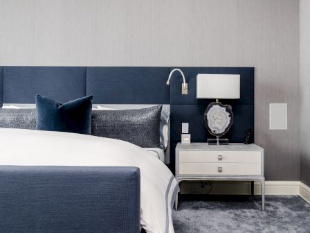 A modern bedroom with a navy and white color scheme, featuring a bed, a nightstand with a lamp, and decorative elements.