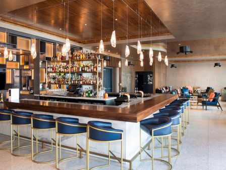A stylish bar with modern seating, a well-stocked liquor display, unique lighting, and a cozy lounge area in the background.