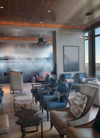 A modern lounge area with comfortable seating, large windows offering a scenic view of water and a Ferris wheel, and ambient lighting.