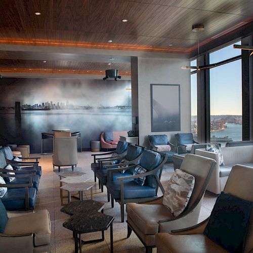 A lounge with plush seating, a wall mural, and large windows offering views of the waterfront and Ferris wheel, providing a cozy atmosphere.