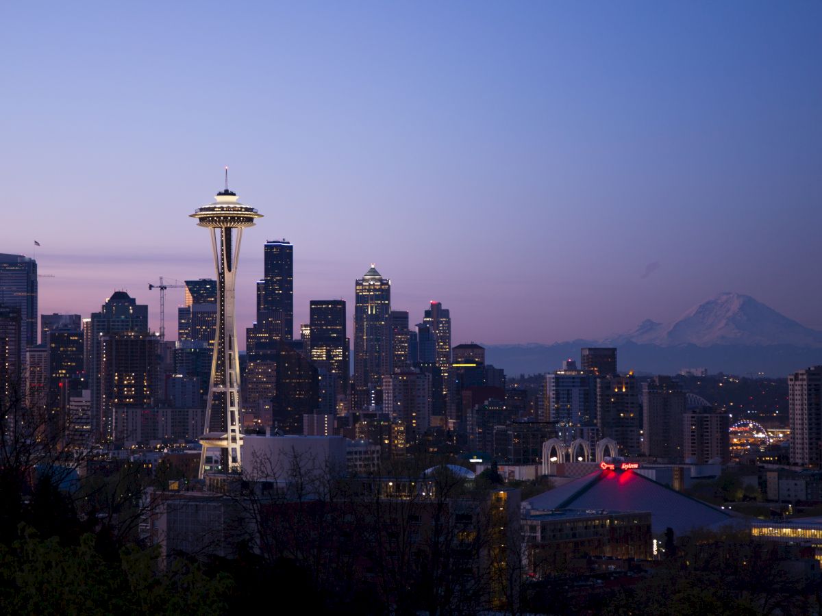 A view of Seattle's skyline at dusk, featuring the Space Needle and Mount Rainier in the background, with a clear, colorful sky.