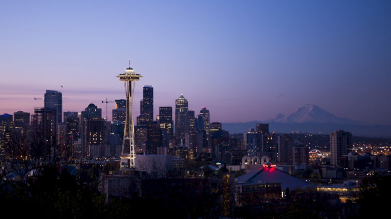 A view of Seattle's skyline at dusk, featuring the Space Needle and Mount Rainier in the background, with a clear, colorful sky.
